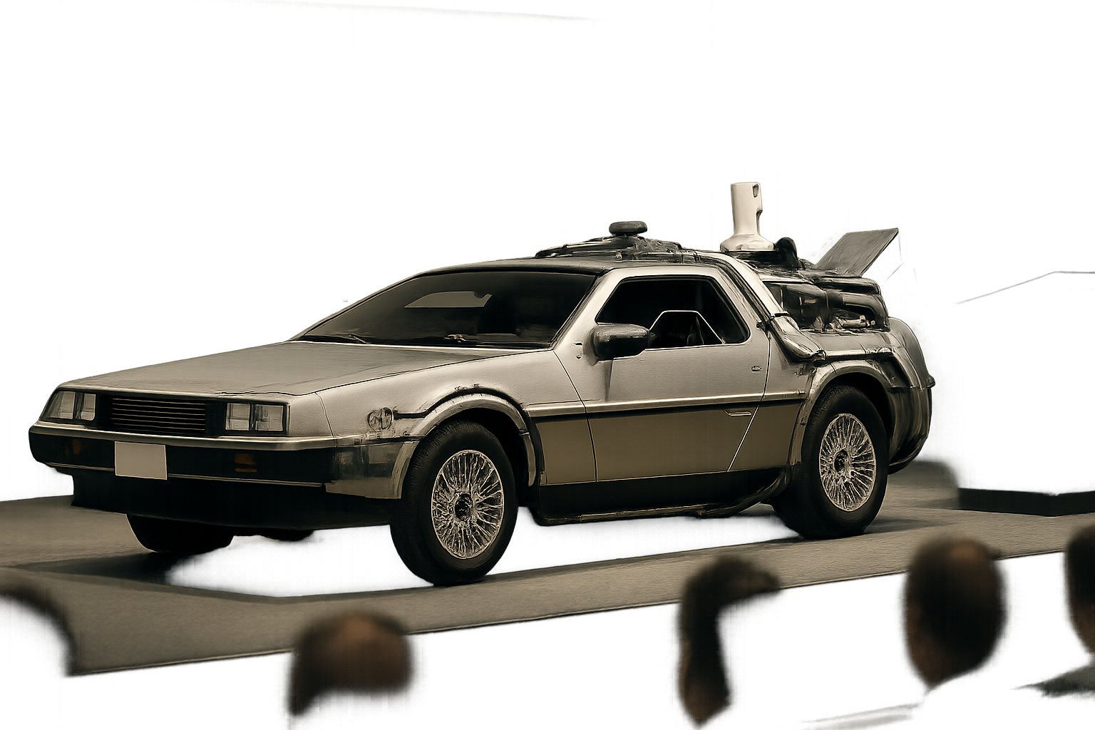 Futuristic silver car with gullwing doors and exposed gadgets on a stage under soft, diffused lighting, audience in foreground