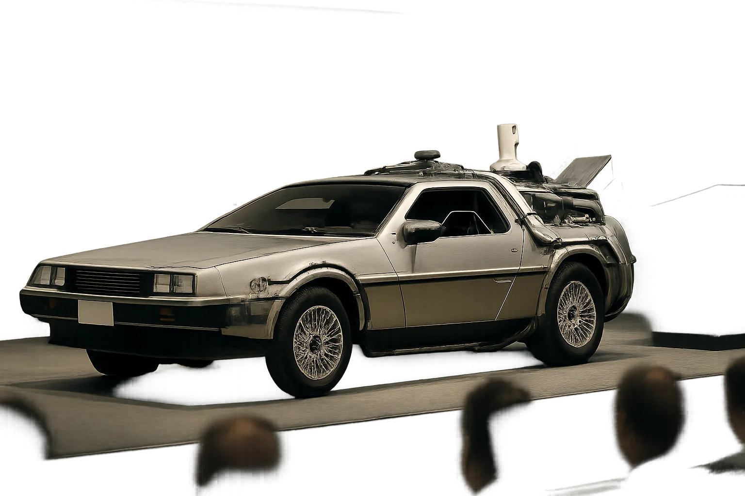 Futuristic silver car with gullwing doors and exposed gadgets on a stage under soft, diffused lighting, audience in foreground